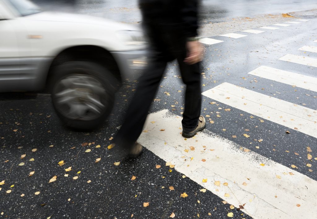Blurred image of a man crossing the street with a car about to hit him