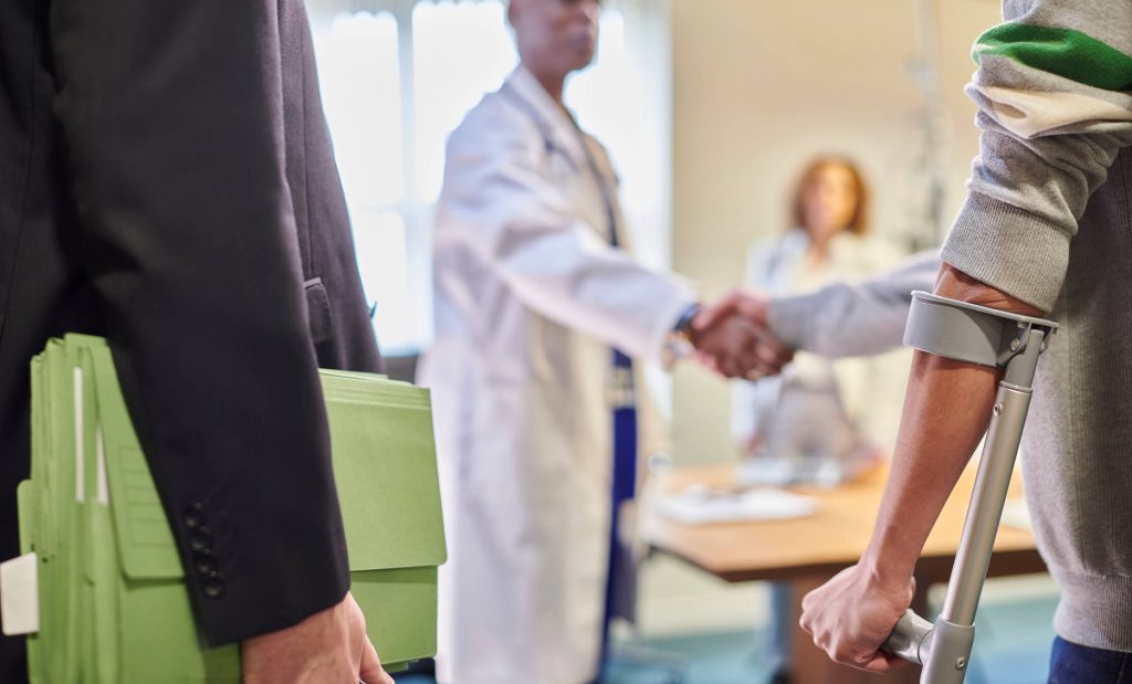 Blurred image of a doctor shaking hands with an injured man and his lawyer carrying a green accordion file.
