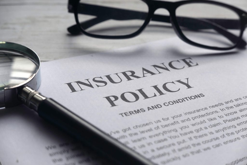 Close-up of an insurance policy with eyeglasses and a magnifying glass on top.