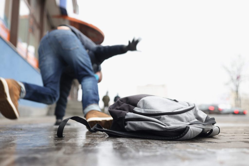 Rear view of someone slipping and falling on ice with their backpack on the ground