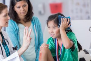 Female ER doctor holds up three fingers while talking with young injured female soccer player holding an ice pack to her head.