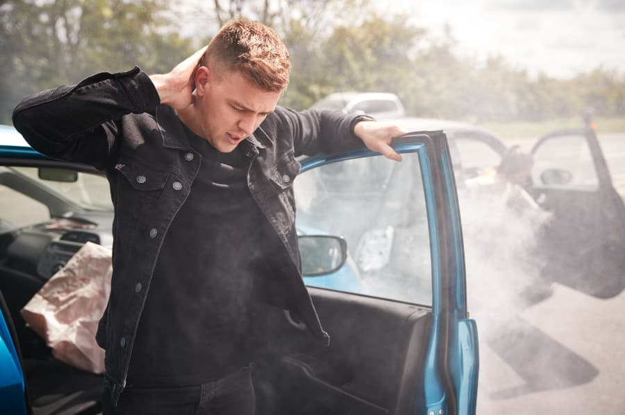Man with whiplash holding his neck getting out of a car after a crash.