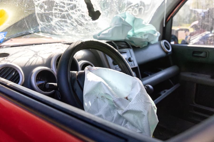 The interior of a wrecked car with deployed airbags and a broken windshield