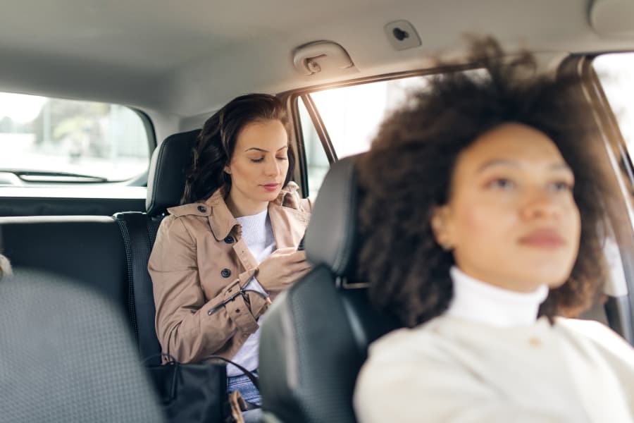 Blurred image of a female Uber driver with a woman in the backseat looking at her phone.